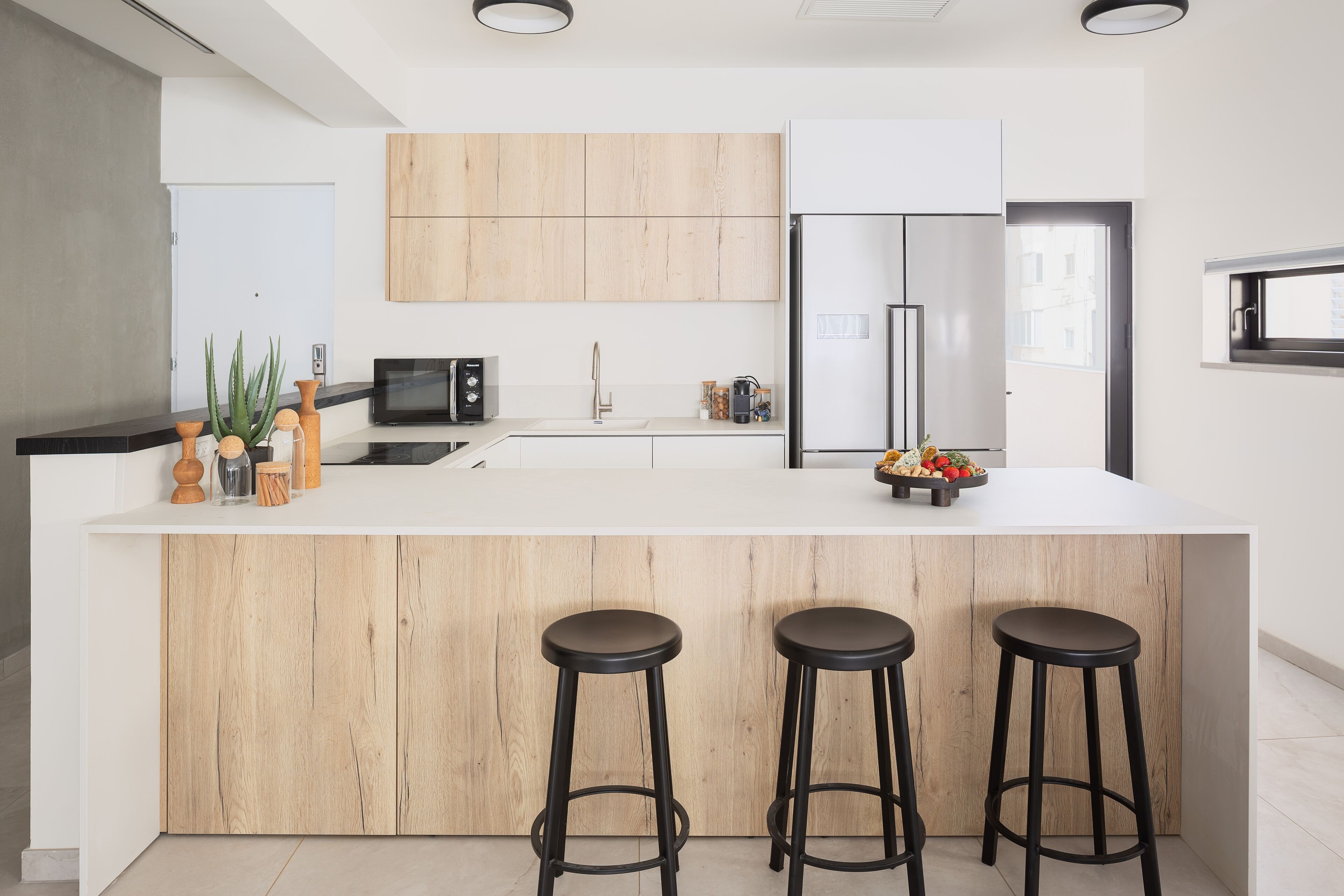 Una cocina moderna con una isla de madera, taburetes, un refrigerador y un microondas.