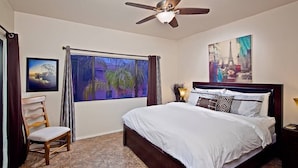A bedroom with a bed, a ceiling fan, a window with curtains, a chair, and artwork on the walls. - Arizona Hideaway (Scottsdale)