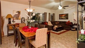 A living room with a dining table, chairs, a sofa, and a coffee table. There is a ceiling fan and a chandelier. - Arizona Hideaway (Scottsdale)