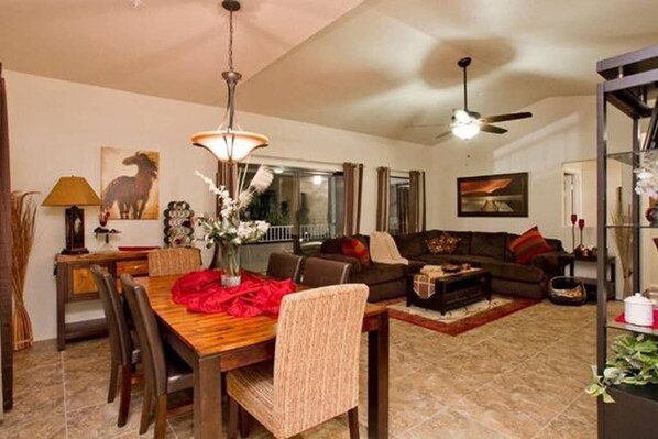 A living room with a dining table, chairs, a sofa, and a coffee table. There is a ceiling fan and a chandelier.