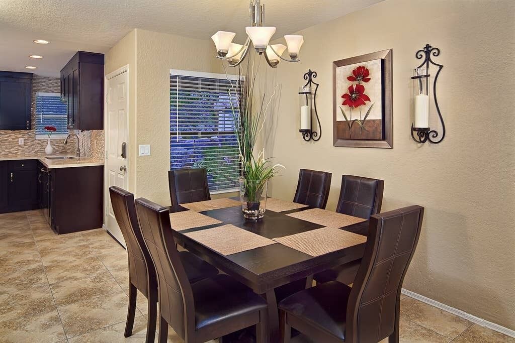 A dining area with a rectangular table, six chairs, a vase with a plant, and wall-mounted light fixtures.