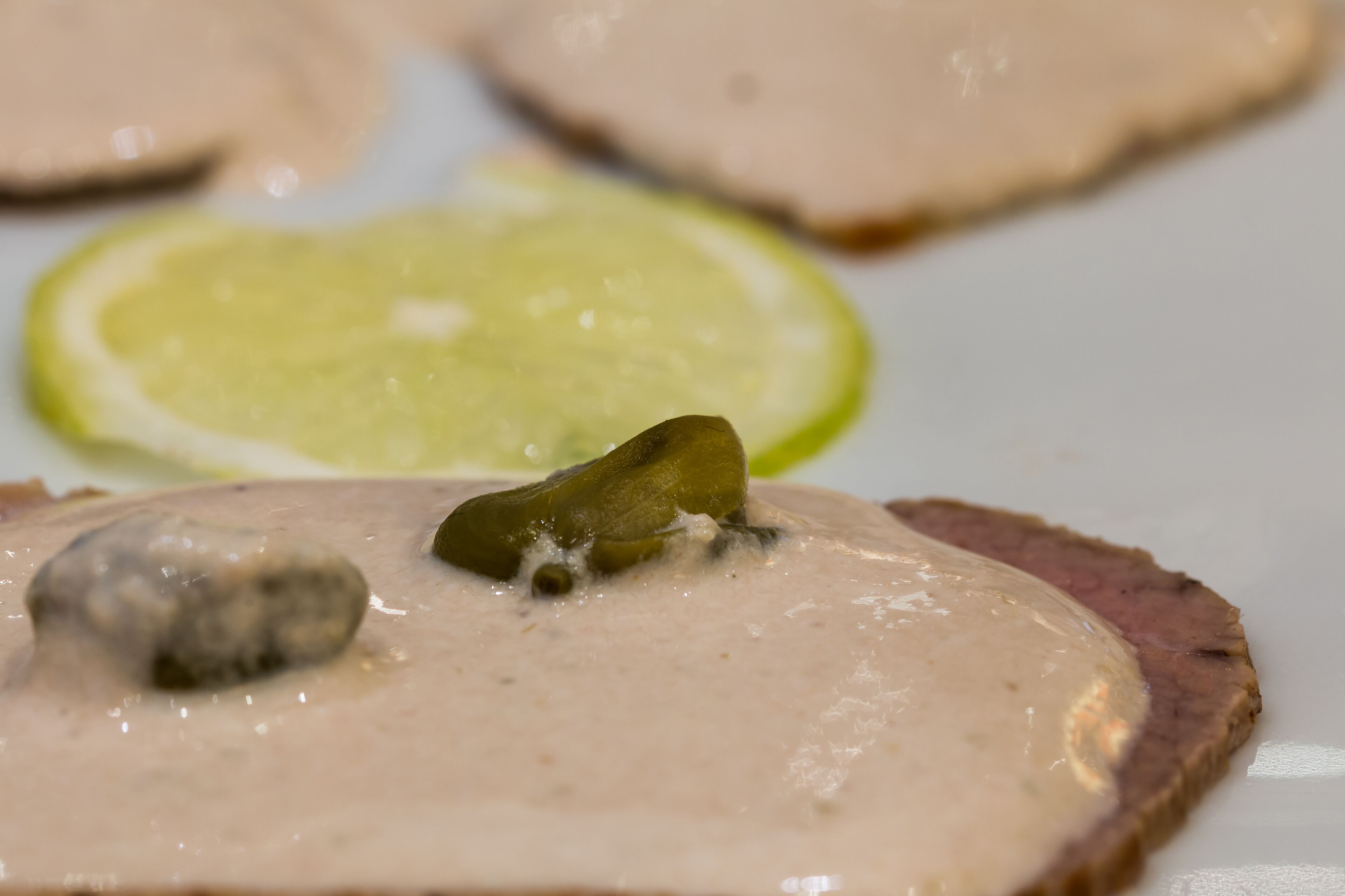 Un plato con lonchas de carne cubiertas con salsa cremosa y una rodaja de lima.