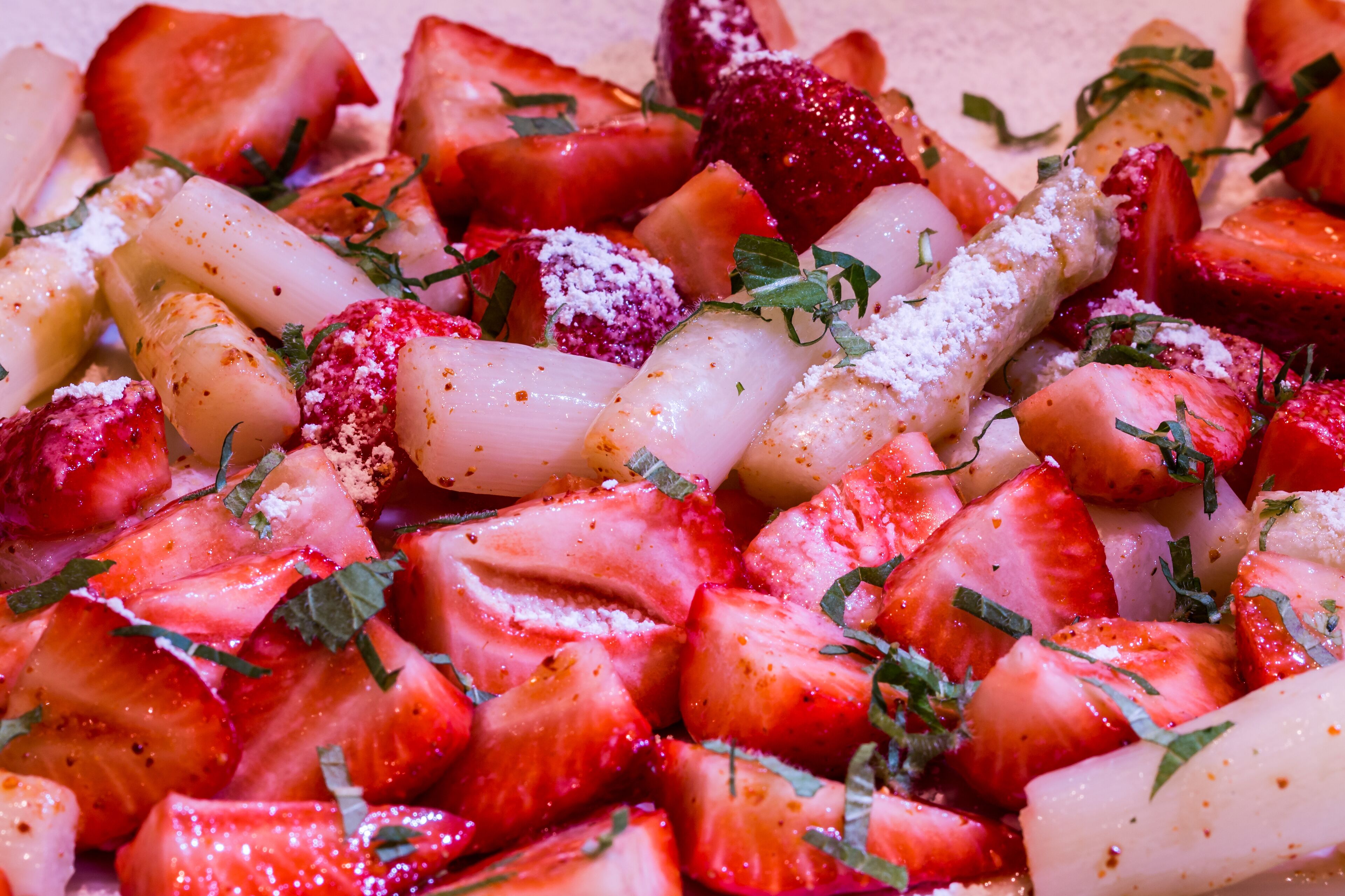 Une vue rapprochée d’une salade de fruits contenant des fraises, des kiwis et des herbes aromatiques.