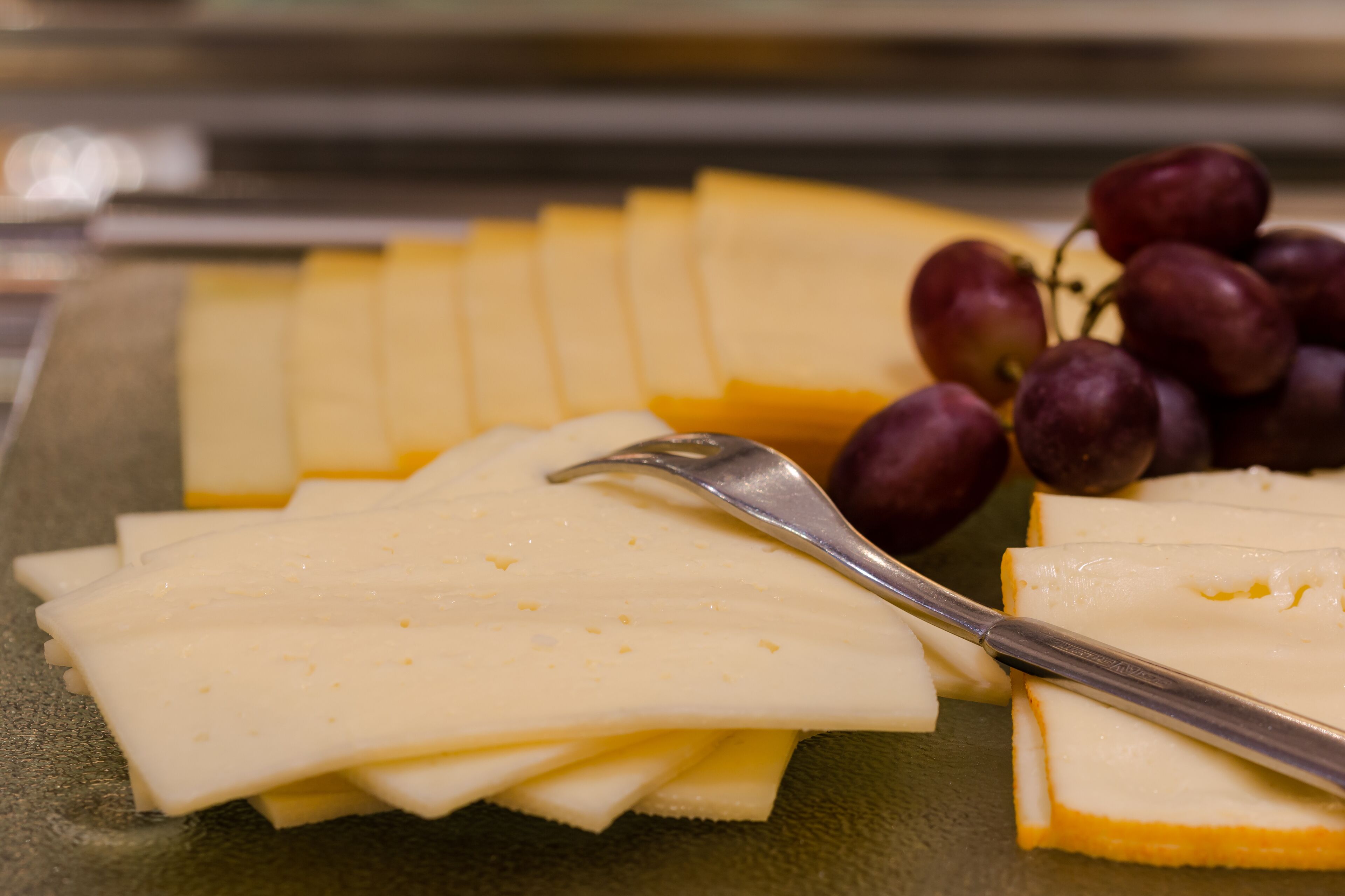 A cheese platter with various types of cheese and grapes on a green plate.