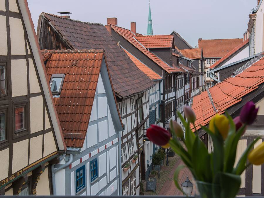 A narrow street lined with traditional half-timbered buildings, a church spire, and a window with a view of the street.