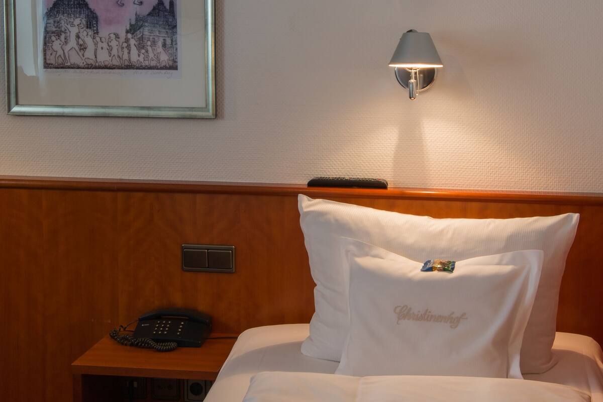 A hotel room with a neatly made bed, a framed artwork on the wall, a bedside lamp, and a telephone on the nightstand.