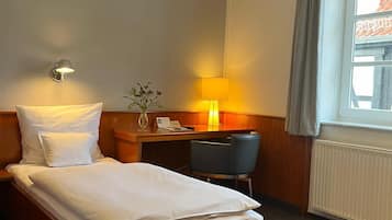 A hotel room with a bed, a desk, a chair, a lamp, and a window with curtains.
