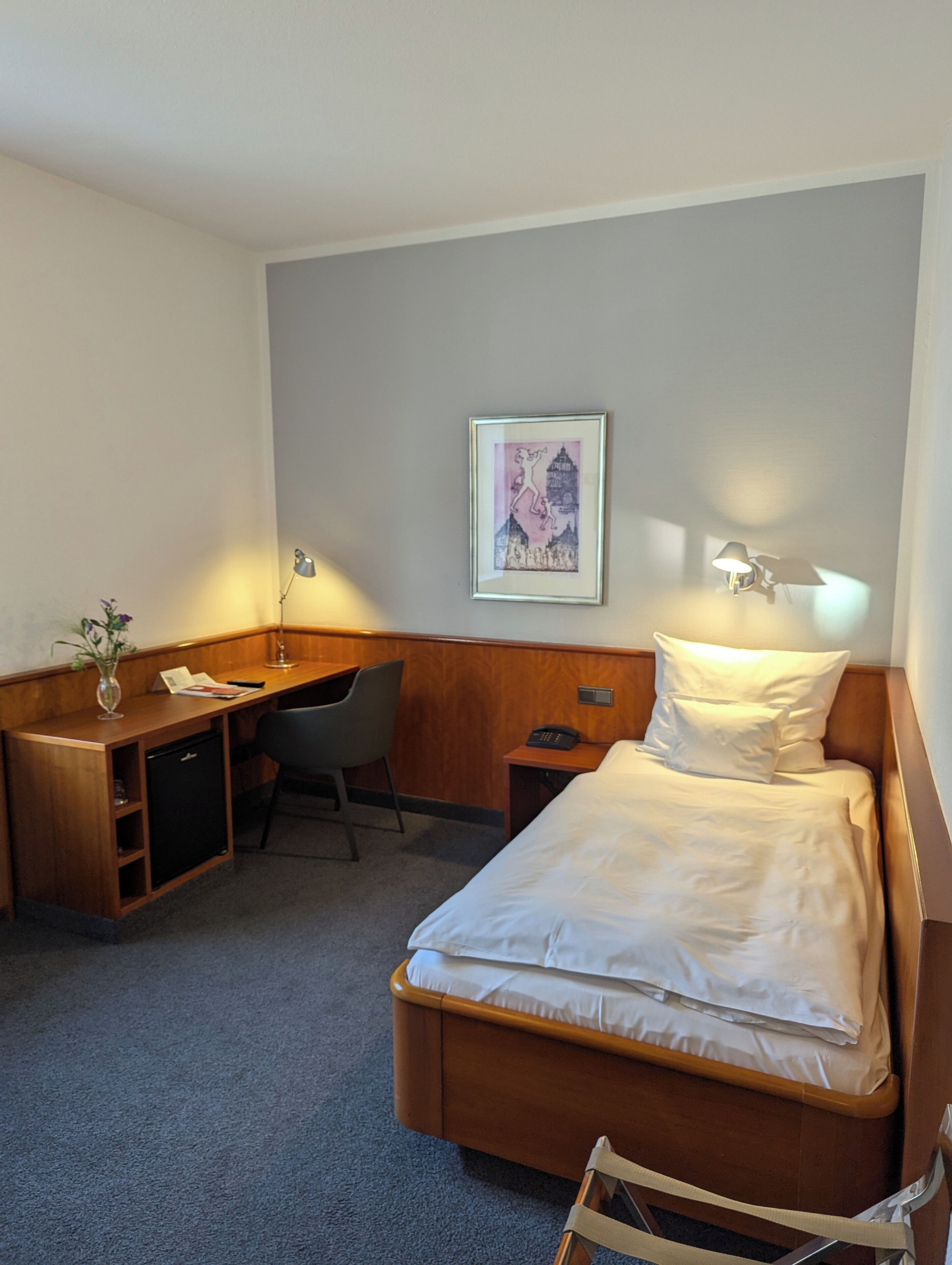 Een hotelkamer met een bed, bureau, stoel en een kleine tafel met lamp.