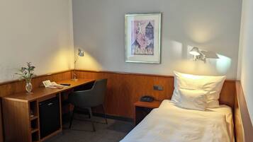 Een hotelkamer met een bed, bureau, stoel en een kleine tafel met lamp.