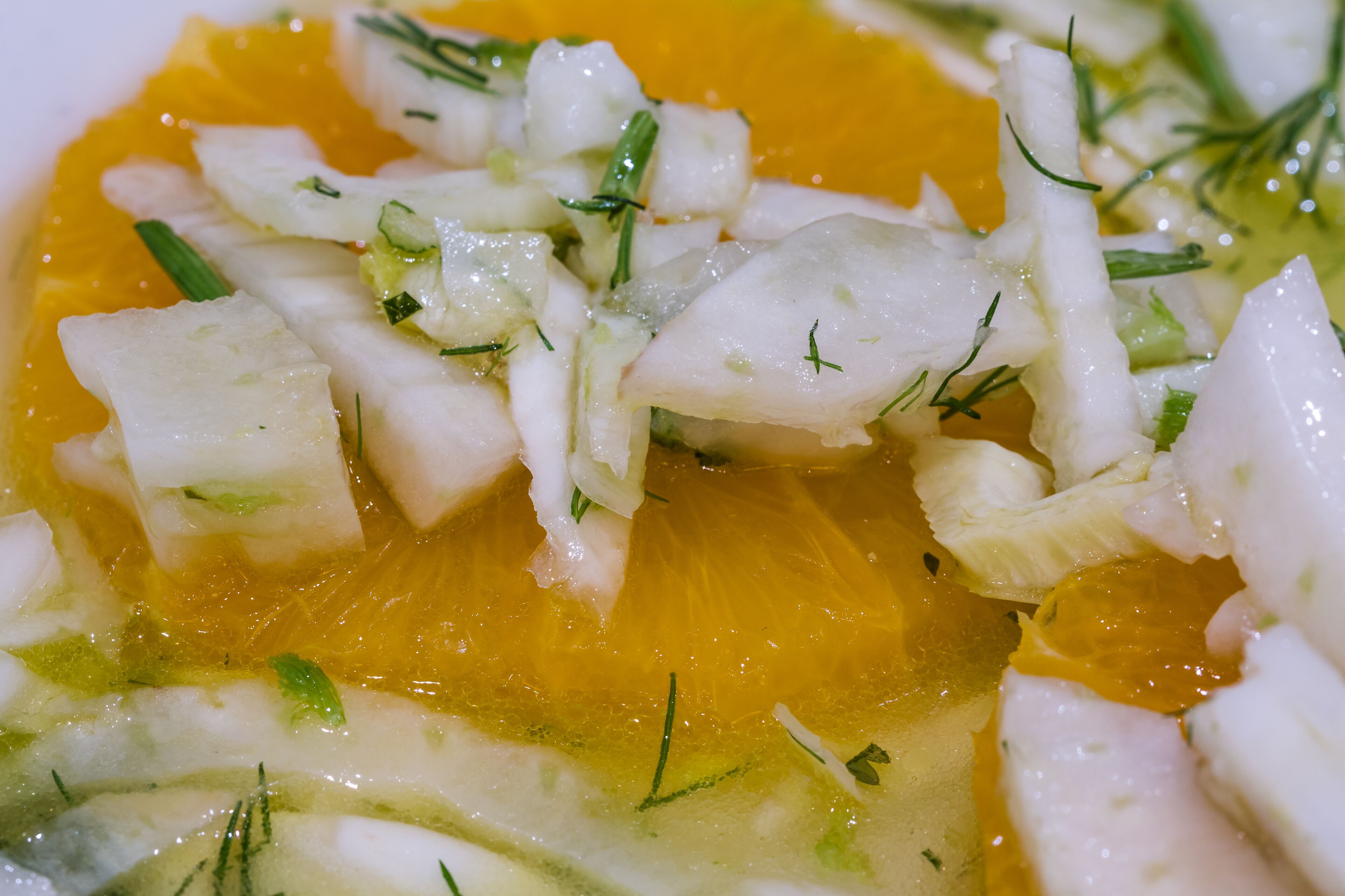 A close-up of a dish with white fish, green herbs, and a yellow sauce.