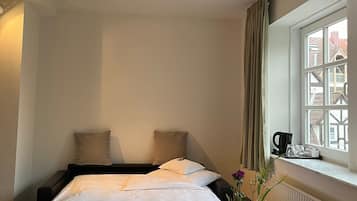 Habitación de hotel con cama, mesita de noche con un florero, ventana con cortinas y vistas a edificios.
