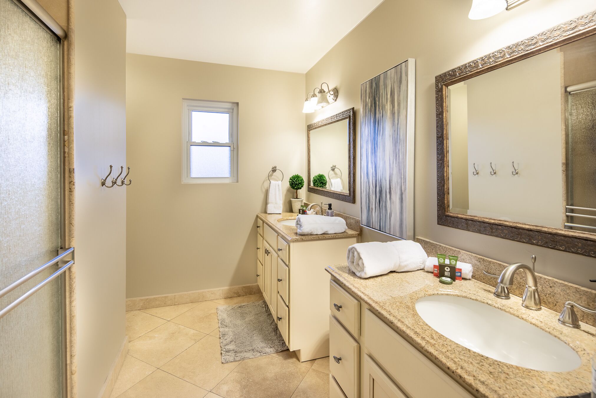 A bathroom with a large sink, vanity, and a mirror. There is a window and a towel rack.