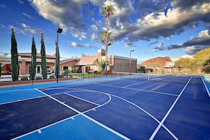 An outdoor basketball court with a clear sky, palm trees, and buildings in the background.
