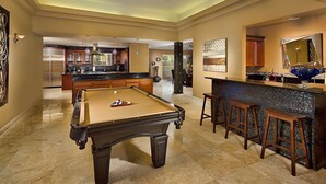 Ein großzügiger Wohnbereich mit Poolbillard, einer Bar mit Hockern und einer Küche im Hintergrund.