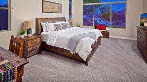 Quarto com cama grande, mesa de cabeceira, cômoda e janela com vista para um estacionamento.