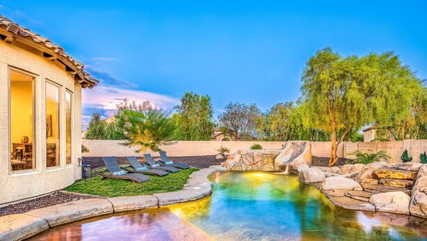 Uma área de piscina com espreguiçadeiras, um recurso aquático de pedra e um edifício com janelas amplas.