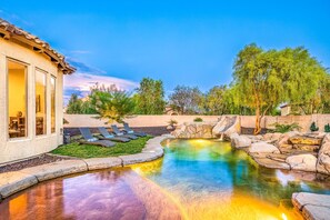 A pool area with lounge chairs, a stone water feature, and a building with large windows. - Desert Hills Estate (Phoenix)