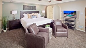 A hotel room with a bed, two chairs, a desk with a TV, and a ceiling fan. - Arizona Desert Haven (Scottsdale)