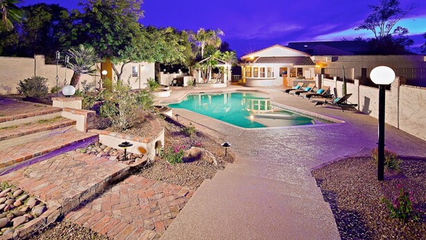 A pool area with lounge chairs, a small gazebo, and a building with a tiled roof. - Arizona Desert Haven (Scottsdale)