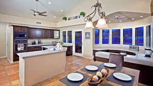 A modern kitchen with a central island, dark wooden cabinets, and a dining area with a wooden table set for four. - Arizona Desert Haven (Scottsdale)