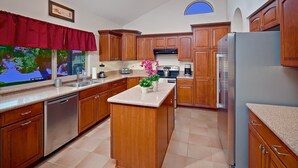 A kitchen with wooden cabinets, a granite countertop, a built-in dishwasher, a refrigerator, and a window with a red valance. - Tatum Place (Phoenix)