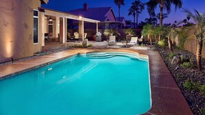 A swimming pool with a covered patio area, palm trees, and a house in the background. - Kierland Retreat (Scottsdale)