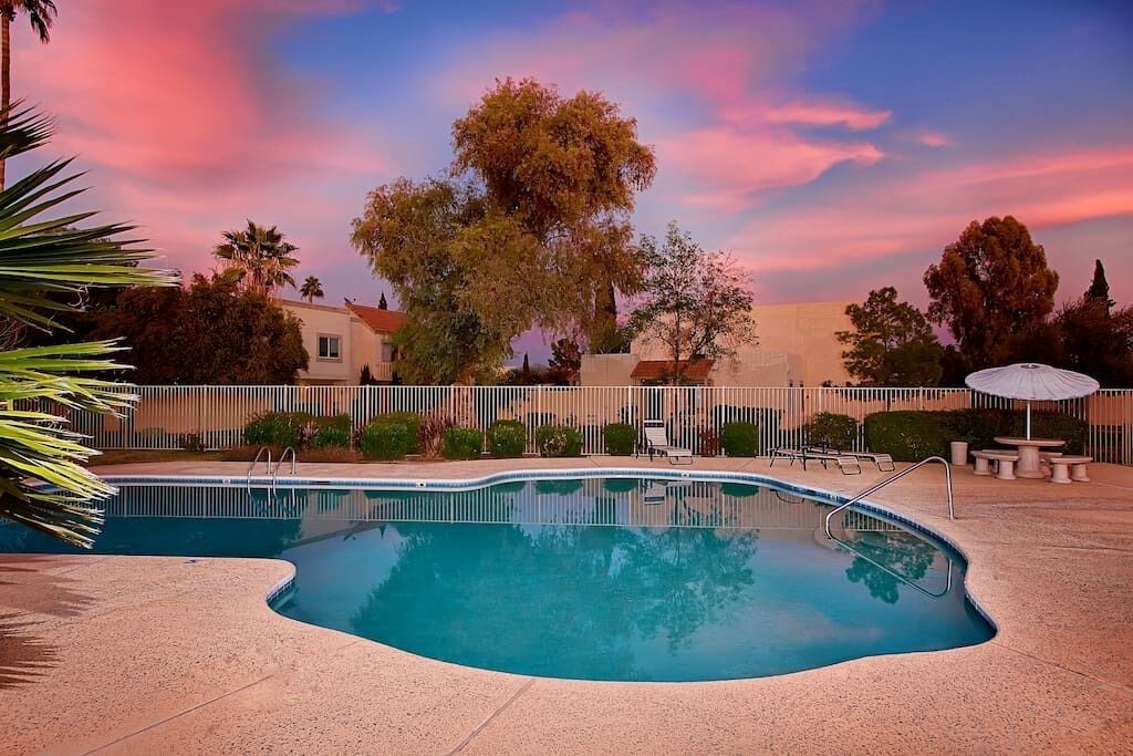 A swimming pool with a curved edge, surrounded by a white fence, and a patio area with outdoor furniture.