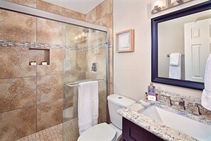 A bathroom with a glass-enclosed shower, a white toilet, and a marble sink with a large mirror. - Silverado Townhouse (Scottsdale)