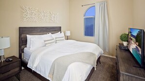 Une chambre à coucher avec un grand lit, une table de chevet avec une lampe, un téléviseur posé sur un meuble en bois et une fenêtre avec des rideaux.