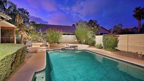 Une piscine entourée de chaises longues, elle-même bordée d’un jardin aménagé et d’un bâtiment doté d’un toit en tuiles.