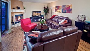 A living room with a fireplace, leather sofas, a red armchair, and a television. - Tempe Escape · Prime Location, Sparkling Pool, Bbq, Tennis Court (Tempe)