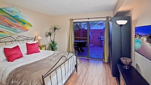 A bedroom with a bed, a TV, a plant, and a sliding glass door leading to an outdoor area. - Tempe Escape · Prime Location, Sparkling Pool, Bbq, Tennis Court (Tempe)