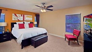 A bedroom with a bed, a ceiling fan, a window with blinds, a red chair, and a desk with a keyboard. - Kierland Getaway (Scottsdale)