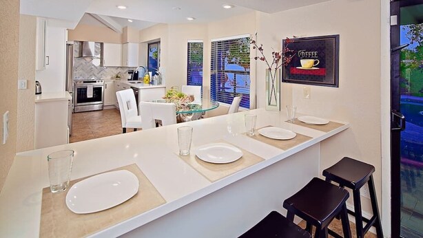 A modern kitchen with a central island, white cabinetry, and a dining area with a glass table and chairs. - Kierland Getaway (Scottsdale)
