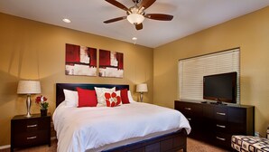 Une chambre à coucher comprenant un lit, des tables de chevet, une commode, un téléviseur et un ventilateur de plafond.