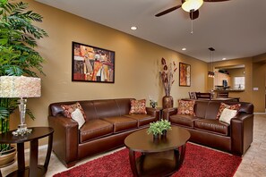 A living room with a brown leather sofa, a coffee table, a red rug, and a ceiling fan. - Paradise View Condo (Scottsdale)
