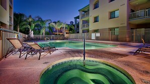 Un espace piscine comprenant des chaises longues, un jacuzzi et un panneau indiquant une zone où il faut faire preuve de prudence.
