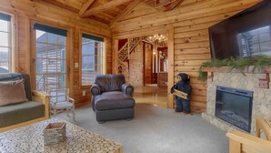 A log cabin interior with a fireplace, a leather armchair, a wooden bear decoration, and a stone fireplace surround.