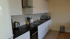 Una cocina moderna con gabinetes blancos, encimera negra, electrodomésticos de acero inoxidable y un cubo de basura.