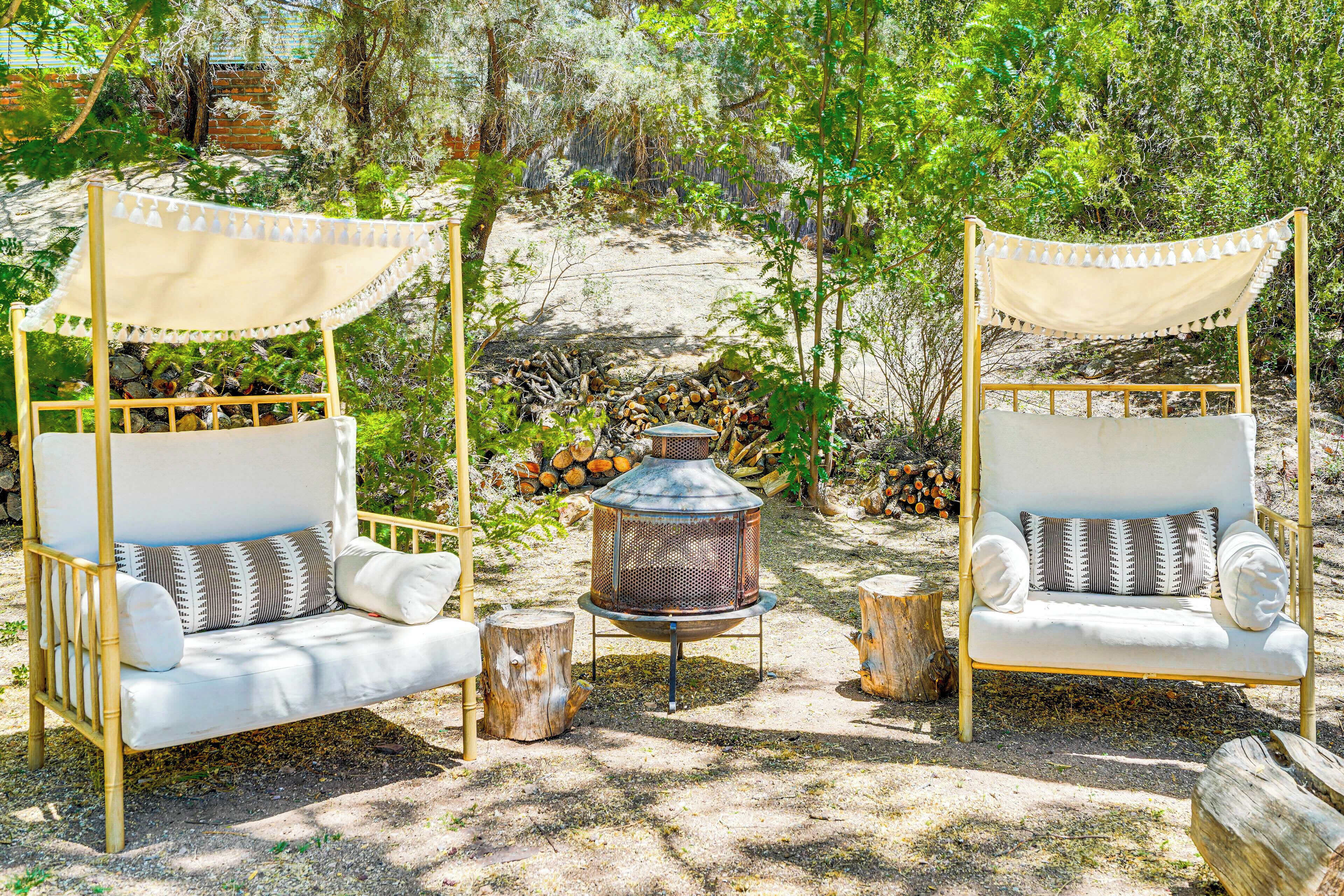 Deux chaises à bascule blanches, dotées de coussins et de toiles de protection, une lanterne en métal et une pile de bûches, le tout dans un décor de jardin.
