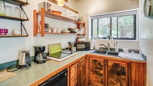 Una cocina con armarios de madera, cafetera, microondas y ventana con vista a árboles.