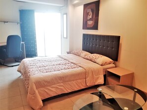 A bedroom with a bed, a desk, a chair, a glass table, and a painting on the wall. - Sea View Studio Jomtien Beach - Sleeps 2 (Pattaya)