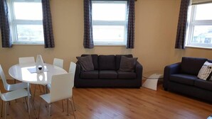 A living room with a dark grey sofa, a white round table with chairs, and a wooden floor.
