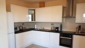 A modern kitchen with white cabinets, a black countertop, a stainless steel range hood, and a built-in oven.