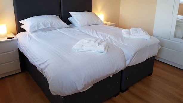 A neatly made double bed with white linens, two bedside tables with lamps, and a window with a view.