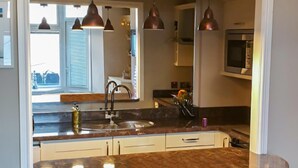 Une cuisine dotée d’un plan de travail en marbre, d’un évier en acier inoxydable et de luminaires suspendus.