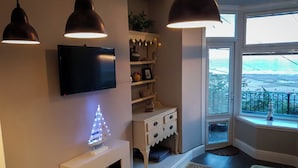Un salon avec un téléviseur, un petit sapin de Noël, un meuble blanc et une fenêtre donnant sur l’extérieur.