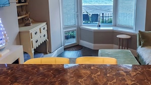 Une chambre avec un bow-window, un lit, une petite table et une commode.