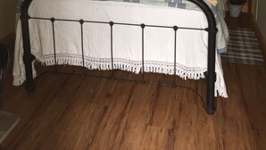 A bed with a metal frame, a white and blue patterned bedspread, and a pillow with the text "my happy place". There is a shelf with plants and a sign that says "RELAX REFRESH RENEW".