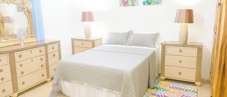 A bedroom with a bed, two bedside tables, a dresser, and a colorful rug.